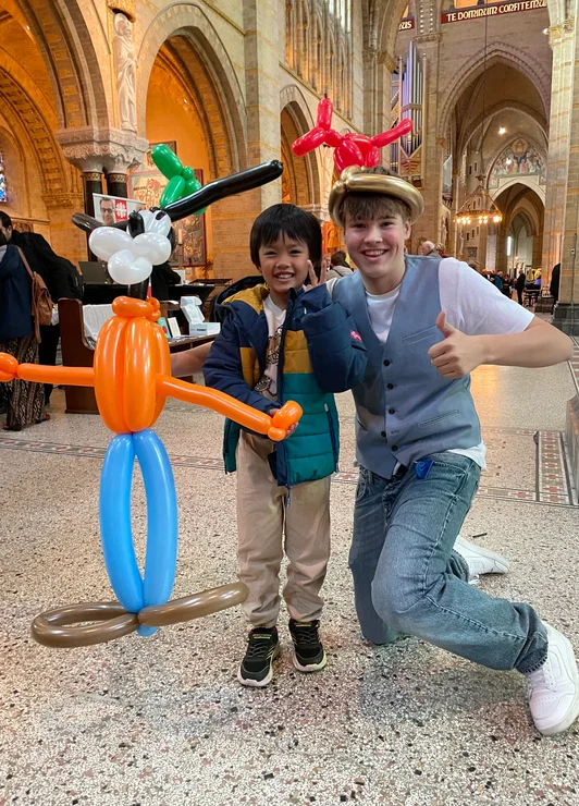 Sem poseert met een kind en kleurrijke ballonfiguren in een kerk.