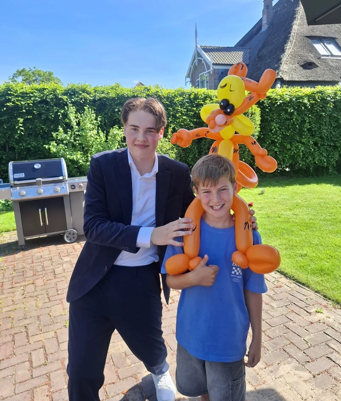 Sem met een kind dat een grote oranje ballonfiguur draagt in een tuin.